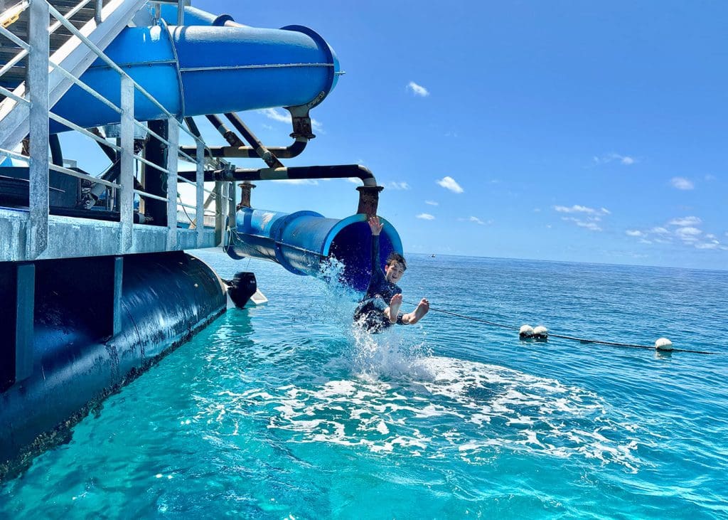 Teenager going down waterslide into the ocean at Sunlover’s Moore Reef pontoon on the Great Barrier Reef