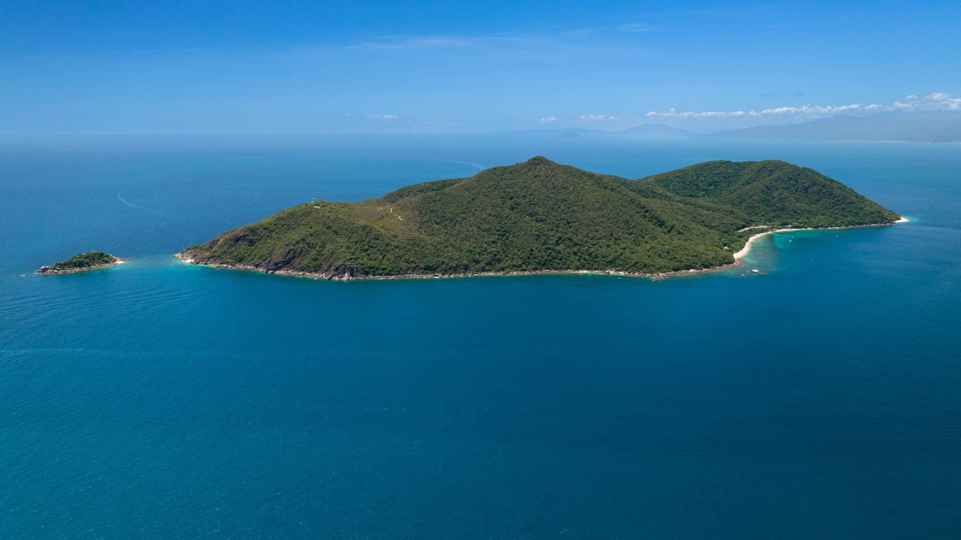 Aerial view of Fitzroy Island's forested granite peak and coral sand beaches surrounded by deep blue water